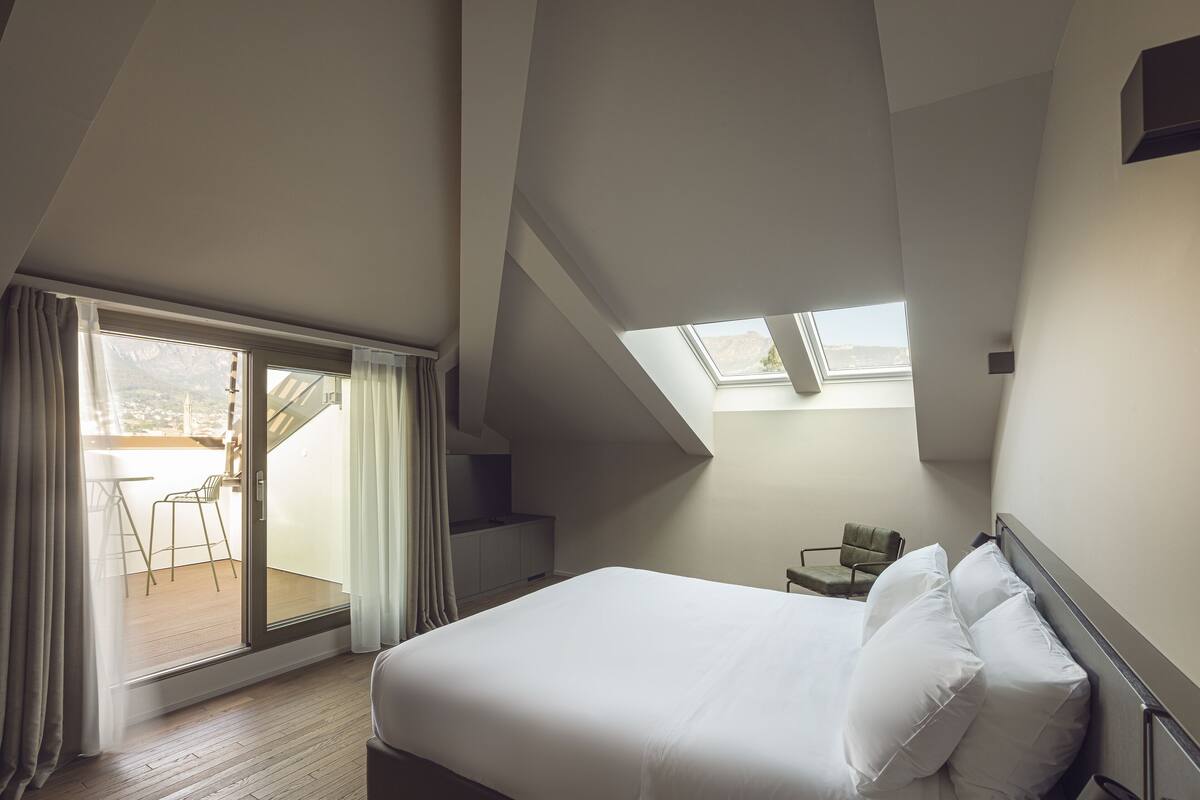 A bedroom with a large bed, a skylight, and a view of an outdoor balcony.