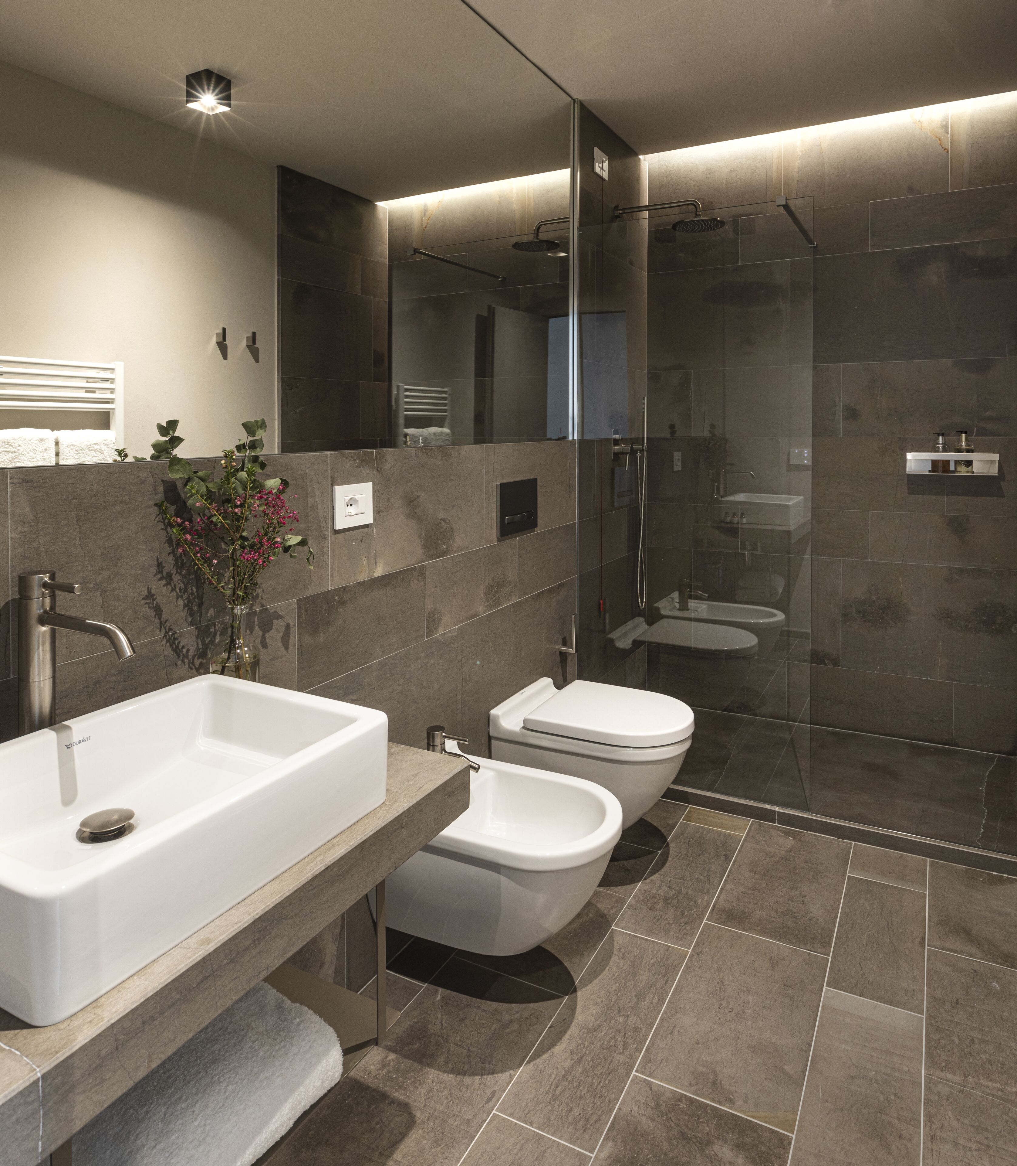 A modern bathroom with a large sink, two toilets, a shower, and a mirror.