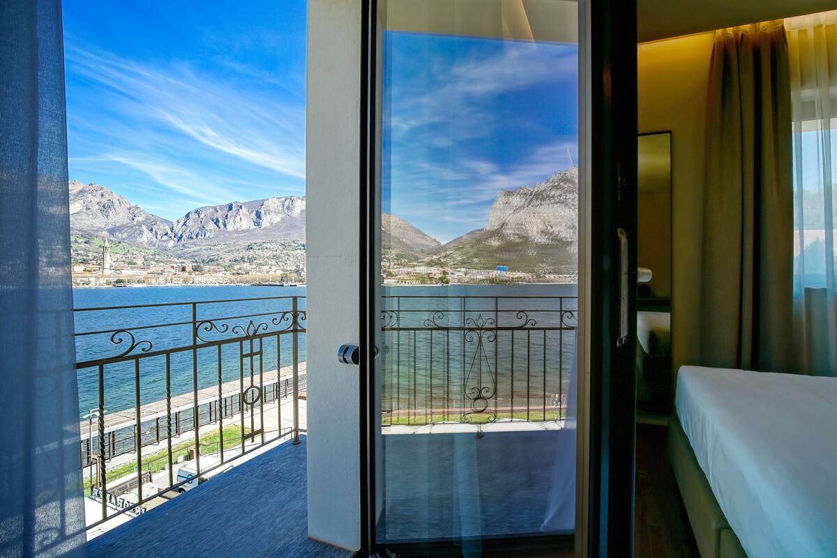 A hotel room with a balcony overlooking a lake and mountains.