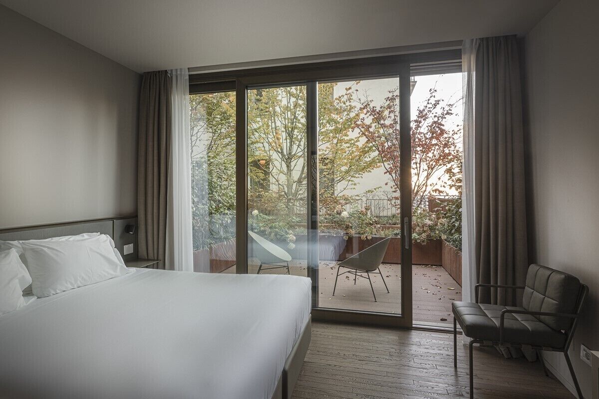 A hotel room with a large bed, a chair, and a view of a balcony with a table and chairs.