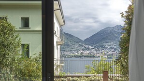 Un balcón con dos sillas modernas, un espacio con césped y vistas a un lago y montañas.
