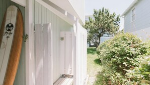 Un bâtiment en bois peint en blanc, doté d’un porche et d’une planche de surf appuyée contre un de ses murs.
