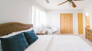 Une chambre à coucher avec un grand lit, un ventilateur de plafond, une table de chevet avec une lampe, une chaise et une armoire.
