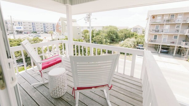 Un balcon avec des balustrades blanches, une chaise blanche avec un coussin rouge et une poubelle blanche.
