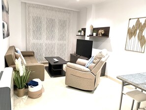 A modern living room with a sofa, a coffee table, a TV, decorative items, and a patterned wall. - LUNA-CENTRAL APARTMENT (Viveiro)