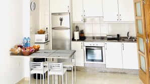 A compact kitchen with white cabinets, a microwave, a refrigerator, a sink, and a dining area with a table and chairs.
