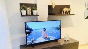 A flat-screen TV on a wooden TV stand with a coastal scene on the screen.