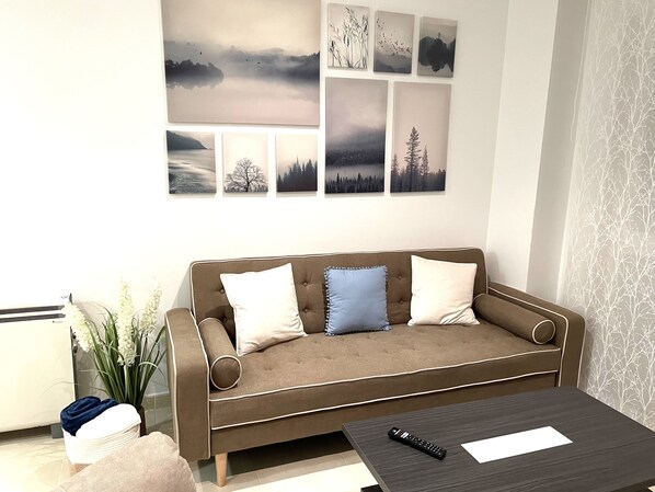 A living room with a brown sofa, two pillows, a remote control, and a vase of flowers. - LUNA-CENTRAL APARTMENT (Viveiro)