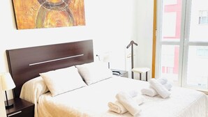 A neatly made bed with white linens and towels, a dark wooden headboard, and a painting on the wall.
