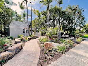 Ein angelegter Eingangsbereich mit einem gewundenen Ziegelweg, der zu einem Gebäude führt, auf dem '999 North Coast Village Entrance & Patrol Office' steht.