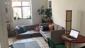 Un espacio de sala acogedor con un sofá, una mesita con una computadora portátil y una planta en maceta.