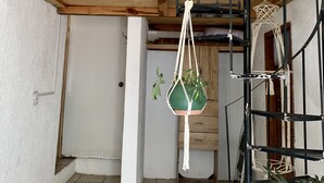 Una habitación pequeña con una litera, una escalera de madera, un colgador de macramé para planta y suelo de baldosas.