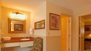 Ett hotellrum med en tvättställsmöbel i badrummet, en stol med ett tyg som har ett naturinspirerat motiv, en säng med ett grönt överdrag och en dörr som leder till ett annat rum.
