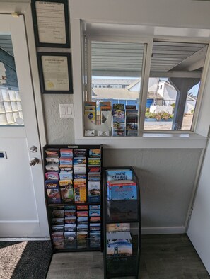 Ein Zimmer mit Fensterblick auf eine Wohngegend, einer Tür sowie einer Auswahl an Reisebüchern und Karten.