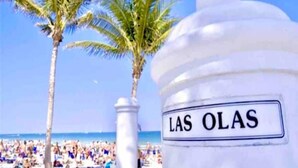 Eine Strandansicht mit Palmen und einem Schild mit der Aufschrift 'LAS OLAS'.