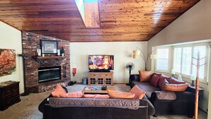Un salon chaleureux avec une cheminée en briques, un téléviseur et des fauteuils confortables.