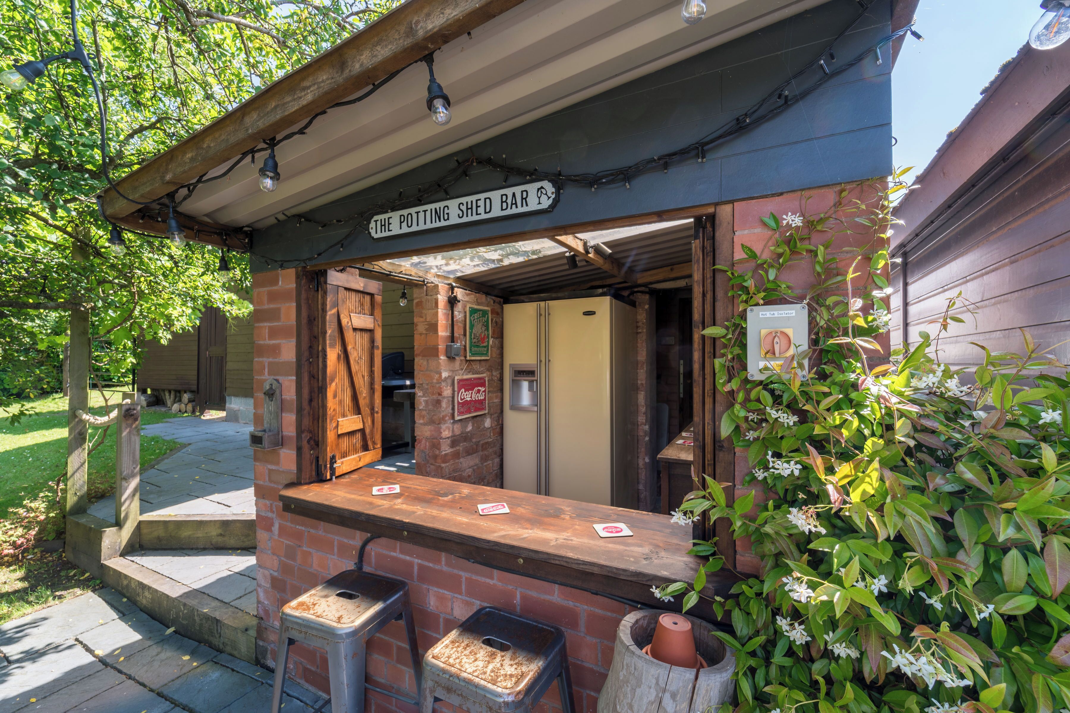 Un bar rústico al aire libre con un letrero que dice 'The Potting Shed Bar', una barra de ladrillo y una puerta de madera.