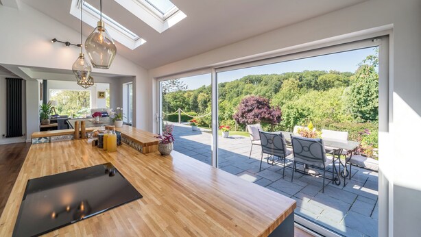 Una cocina moderna con encimera de madera, zona de comedor con asientos exteriores y un amplio ventanal corredera que da a un jardín.