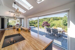 A modern kitchen with a wooden countertop, a dining area with outdoor seating, and a large sliding glass door leading to a garden.