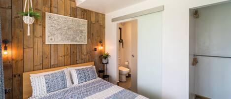 A bedroom with a wooden wall, a bed with patterned bedding, a hanging plant, and a map on the wall.