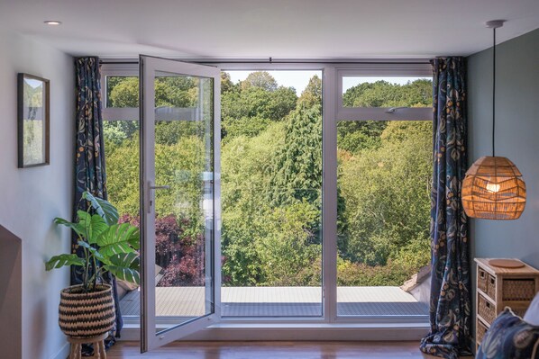 A room with a large sliding glass door leading to a balcony, a potted plant, a woven light fixture, and a small wooden side table.