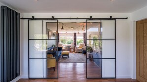 Un interior moderno con un divisor de vidrio corredera que da a una sala de estar con sofás, una mesa de centro y vistas al exterior lleno de vegetación.