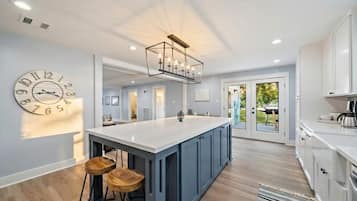 A modern kitchen with a central island, bar stools, and a large clock on the wall.