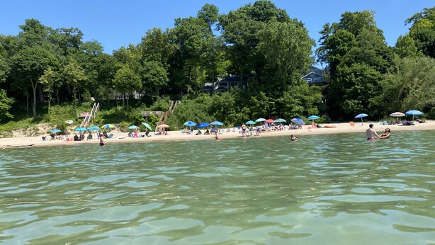 Ein Strand mit klarem Wasser, Sonnenschirmen und Menschen.