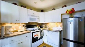A compact kitchen with white cabinets, a microwave, a stove, and a refrigerator. - Cozy Winter Escape (Laconia)