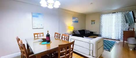 Un área de comedor con una mesa y sillas, un sofá, una lámpara y una ventana con cortinas.