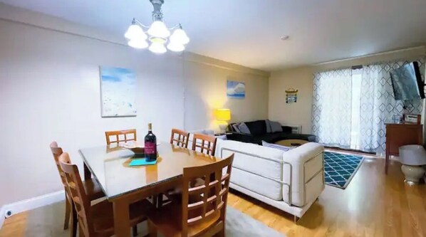 A dining area with a table and chairs, a sofa, a lamp, and a window with curtains.