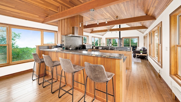 A spacious kitchen with wooden beams, large windows, and a bar area with stools.