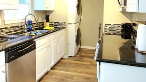 A compact kitchen with white cabinets, a dishwasher, a washing machine, and a microwave. - Duplex with Backyard and Putting Green (Beaverton)