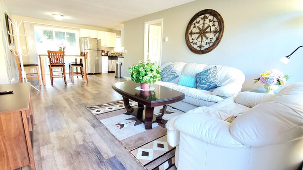 A living room with a sofa, a coffee table with a plant, and a dining area with chairs and a table. - Duplex with Backyard and Putting Green (Beaverton)