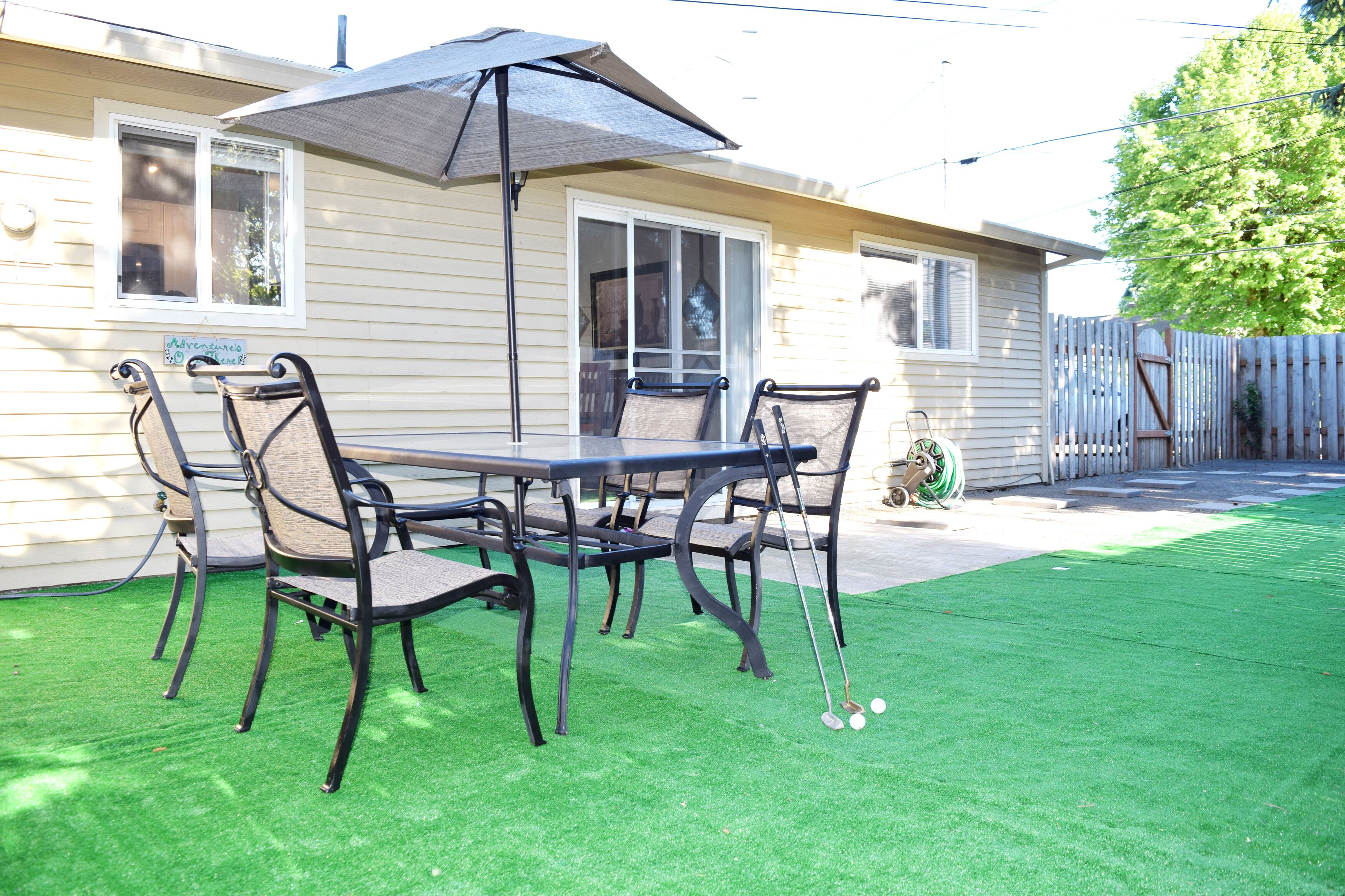 A patio with a table and chairs, a lawn, and a house in the background.
