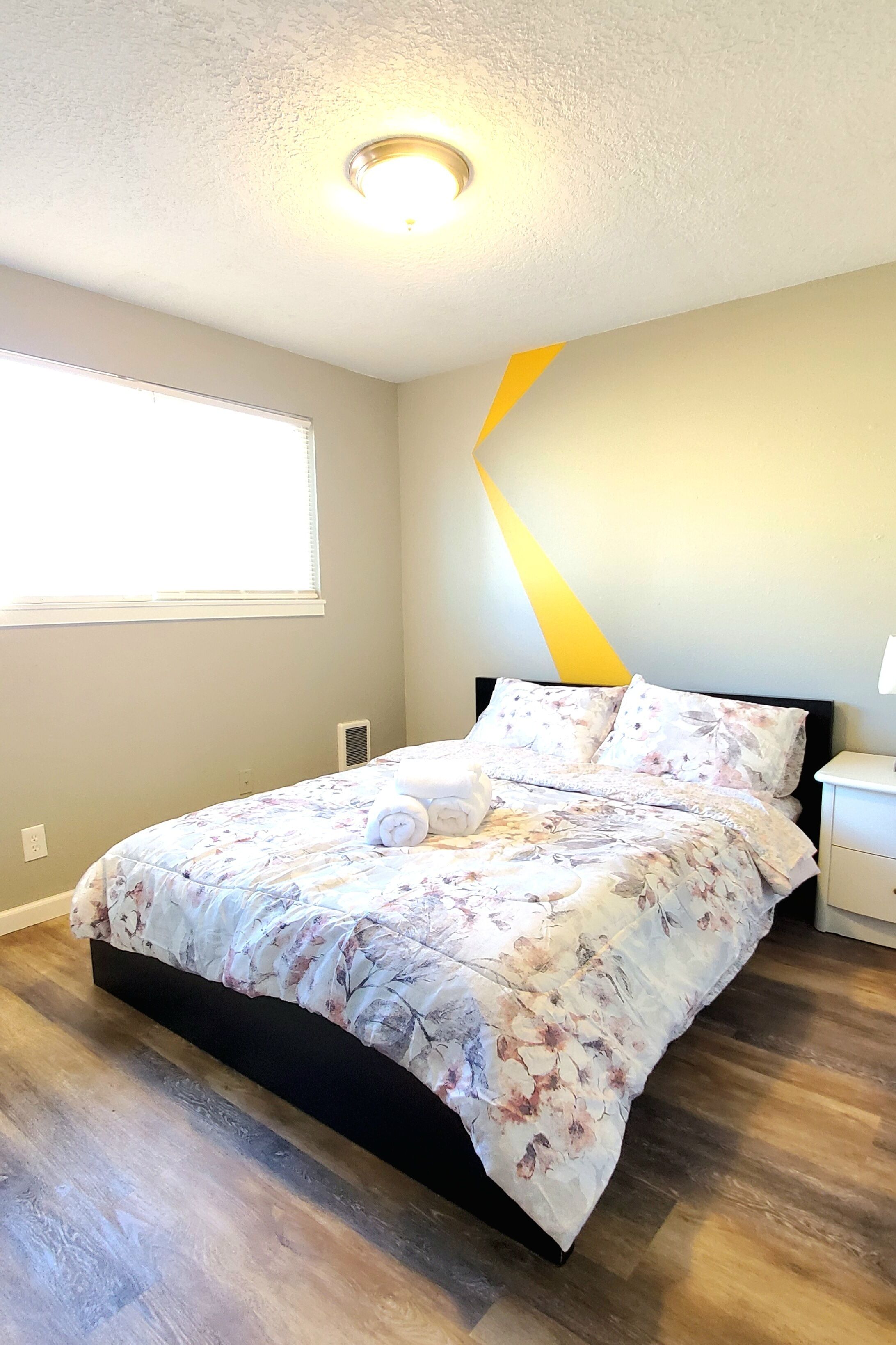 A bedroom with a bed, a nightstand, a lamp, and a window with blinds.