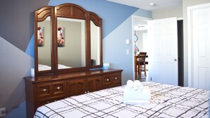 A bedroom with a large bed, a wooden dresser, a mirror, and a door leading to another room. - Duplex with Backyard and Putting Green (Beaverton)
