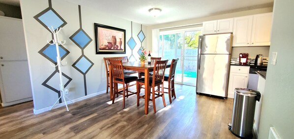 A dining area with a wooden table and chairs, a framed picture on the wall, and a sliding glass door leading to a backyard. - Duplex with Backyard and Putting Green (Beaverton)