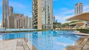 A swimming pool with a tiled edge, surrounded by a paved area and tall residential buildings in the background.