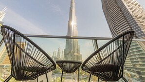 A view of the Burj Khalifa from a balcony with three black wire-framed chairs.