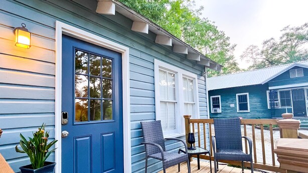 A blue house with a front door, a porch with two chairs, a small table, and a welcome mat.