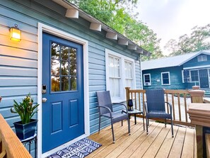A blue house with a front door, a porch with two chairs, and a small table.