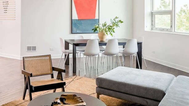 Een moderne woonkamer met een bank, een rond salontafeltje en een eethoek met stoelen en een tafel.