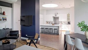Een moderne woonkamer met een donkere accentmuur, een flatscreen televisie en een eethoek met een grote tafel en stoelen.