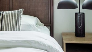Een net opgemaakt bed met een gestreept kussen, een donker hoofdbord en een nachtkastje met een lamp.