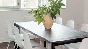 Een moderne eetruimte met een grote tafel, witte stoelen en een potplant.