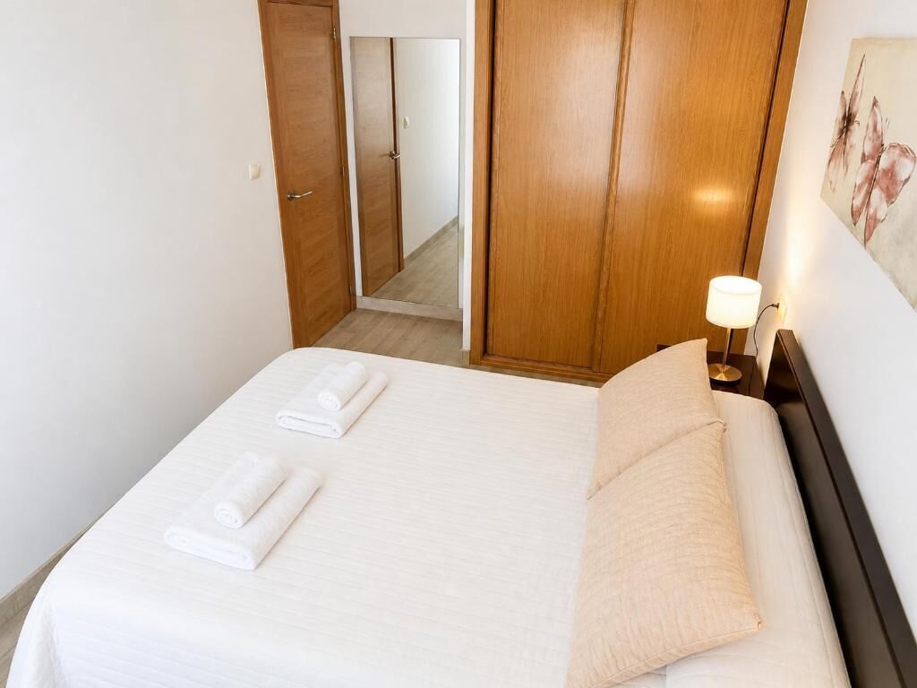 Hotelkamer met een bed, nachtkastje met lamp, houten garderobe en een deur naar een andere kamer.