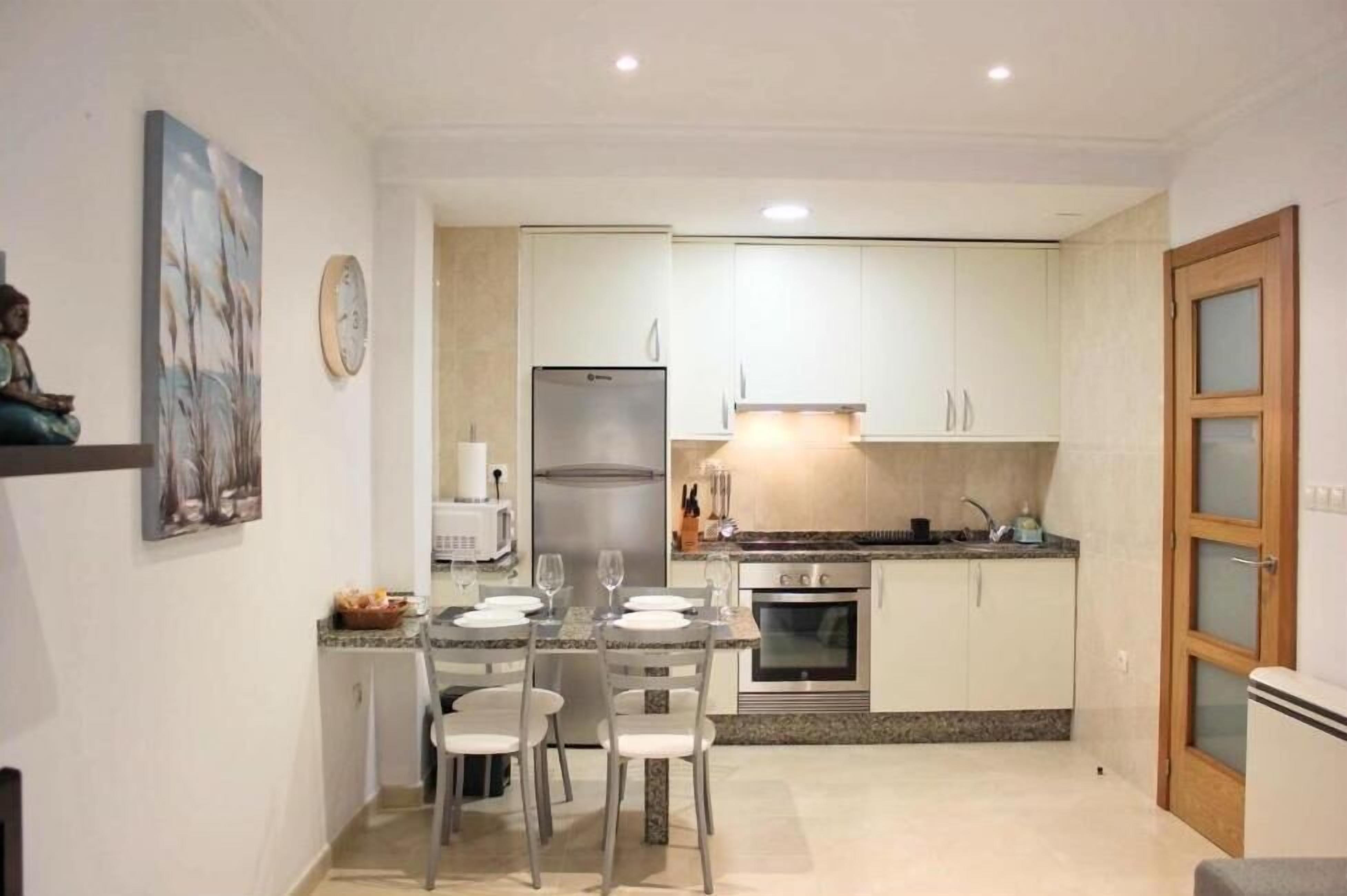 Cocina compacta con comedor, refrigerador, horno y lavamanos.