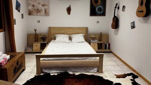 A bedroom with a wooden bed, two bedside tables, a nightstand, a wall-mounted guitar, and a cowhide rug. - Small vacation villa, beach and barbecue :-) (Bastelicaccia)