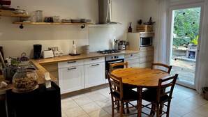 A modern kitchen with white cabinets, a wooden dining table, and a view of a garden through a sliding door. - Small vacation villa, beach and barbecue :-) (Bastelicaccia)